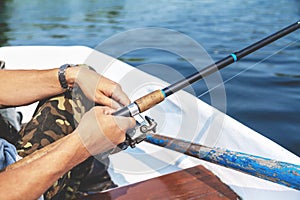 Hands fisherman holding fishing rod and reel handle is rotated