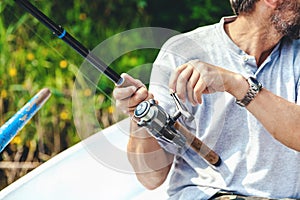 Hands fisherman holding fishing rod and reel handle is rotated