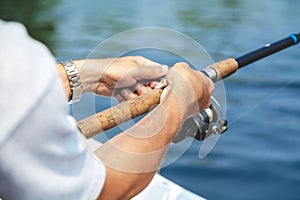 Hands fisherman holding fishing rod and reel handle is rotated