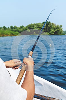 Hands fisherman holding fishing rod and reel handle is rotated