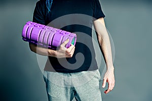 Hands of a fitness trainer man holding a roller for myofascial relaxation on a gray background