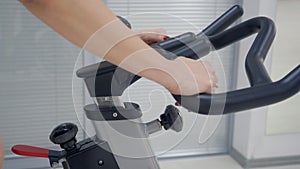 Hands of fitness woman holding handlebar indoor bike adjusting while training