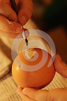 Hands of five years old girl painting yellow heart on blowed easter egg with thin brush