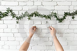 hands fixing starshaped garland on white brick wall photo