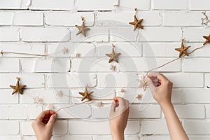 hands fixing starshaped garland on white brick wall photo