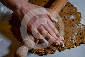 hands flattening a dough of flour, sugar, eggs and chocolate chips with a rolling pin to make biscuits