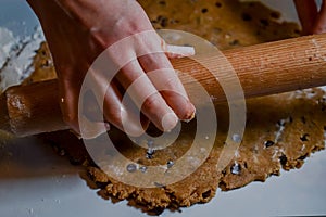 hands flattening a dough of flour, sugar, eggs and chocolate chips with a rolling pin to make biscuits