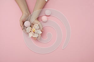 Hands with flower and bath bomb on pink background Spa concept