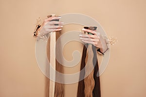 Hands with flowers hold strands of hair for extensions on a beige background.