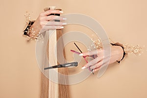 Hands with flowers hold strands of hair for extensions on a beige background.