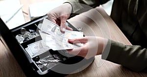 Hands fold banknotes and coins in a mini safe, close-up