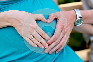 Hands folded mom and dad a heart on pregnant tummy