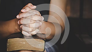 Hands folded in prayer on a Holy Bible in church concept for faith