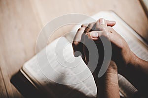 Hands folded in prayer on a Holy Bible in church concept for faith