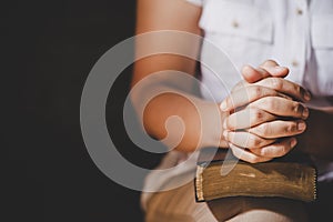 Hands folded in prayer on a Holy Bible in church concept for faith