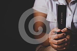 Hands folded in prayer on a Holy Bible in church concept for faith