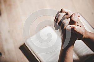 Hands folded in prayer on a Holy Bible in church concept for faith