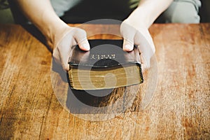 Hands folded in prayer on a Holy Bible in church concept for faith