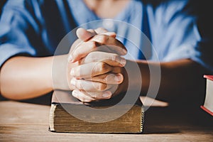 Hands folded in prayer on a Holy Bible in church concept for faith