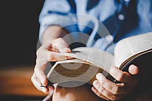 Hands folded in prayer on a Holy Bible in church concept for faith