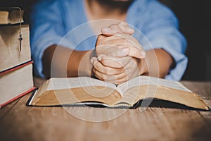 Hands folded in prayer on a Holy Bible in church concept for faith