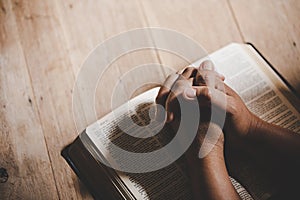 Hands folded in prayer on a Holy Bible in church concept for faith