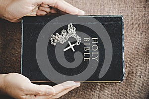 Hands folded in prayer on a Holy Bible in church concept for faith