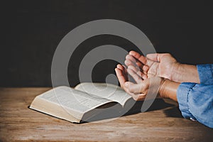 Hands folded in prayer on a Holy Bible in church concept for faith