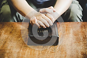 Hands folded in prayer on a Holy Bible in church concept for faith