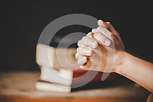 Hands folded in prayer on a Holy Bible in church concept for faith