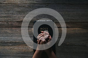 Hands folded in prayer on a Holy Bible in church concept for faith