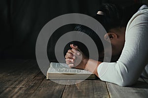 Hands folded in prayer on a Holy Bible in church concept for faith