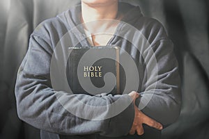 Hands folded in prayer on a Holy Bible in church concept for faith