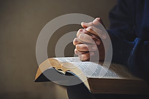 Hands folded in prayer on a Holy Bible in church concept for faith