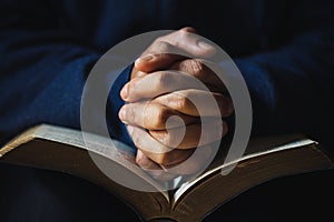 Hands folded in prayer on a Holy Bible in church concept for faith