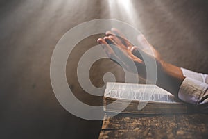 Hands folded in prayer on a Holy Bible in church concept for faith