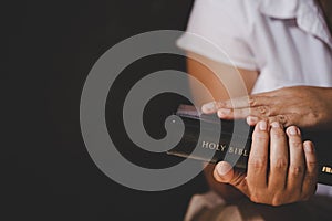 Hands folded in prayer on a Holy Bible in church concept for faith