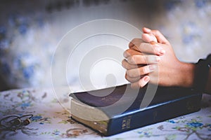 Hands folded in prayer on a Holy Bible in church concept for faith, spirituality and religion, woman praying on holy bible in the