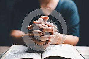 Hands folded in prayer on a Holy Bible in church concept for faith, spirituality and religion, woman praying on holy bible in the