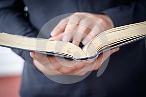 Hands folded in prayer on a Holy Bible in church concept for faith, spirtuality and religion