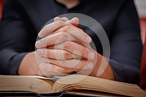 Hands folded in prayer on a Holy Bible in church concept for faith, spirtuality and religion