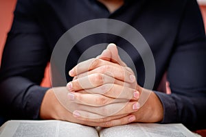 Hands folded in prayer on a Holy Bible in church concept for faith, spirtuality and religion