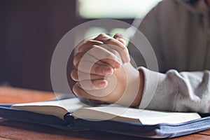 Hands folded in prayer on a Holy Bible in church concept for fa
