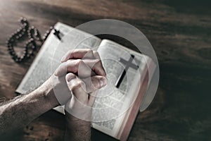 Hands folded in prayer on a Holy Bible in church, faith, spirtuality and religion