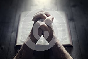 Hands folded in prayer on a Holy Bible in church, faith, spirtuality and religion