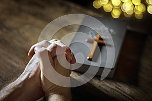 Hands folded in prayer with  Holy Bible and religious crucifix cross in church