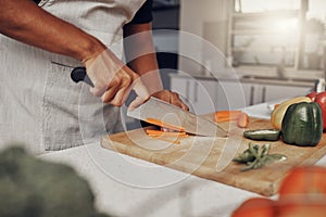 Hands, food and salad with a man cooking in the kitchen, while cutting carrots on a wooden chopping board. Nutrition