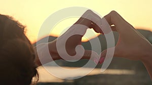 Hands forming a heart shape with sunset silhouette. Ocean sun shining through heart shaped female hands. Love. Nature