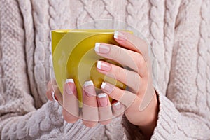 Hands with french manicure holding a yellow mug.