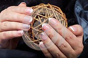 Hands with french manicured nails holding a golden Christmas ball